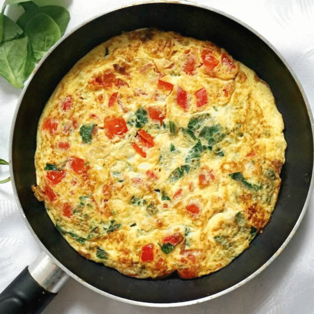 A perfect golden-brown veggie omelette, cut open to show a fluffy interior packed with colorful vegetables and melted cheese.
