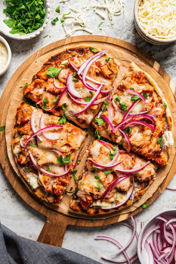 A golden-brown BBQ chicken pizza topped with shredded chicken, melted cheese, red onion, and fresh cilantro—the ultimate sweet and smoky pizza