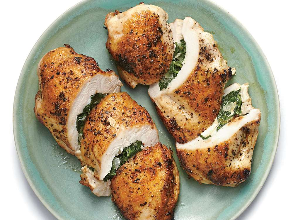 Overhead shot of ingredients for Stuffed Chicken: fresh spinach, block of feta, cream cheese, garlic, and raw chicken breasts on a dark wooden board. The photo is styled to look vibrant and slightly messy, capturing the unpolished preparation phase.
