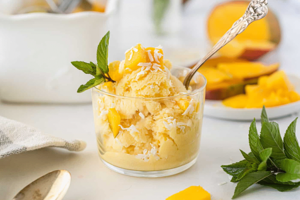 A scoop of vibrant, creamy mango ice cream in a coconut bowl, with a fresh mango slice garnish—your easy, tropical dessert escape.
